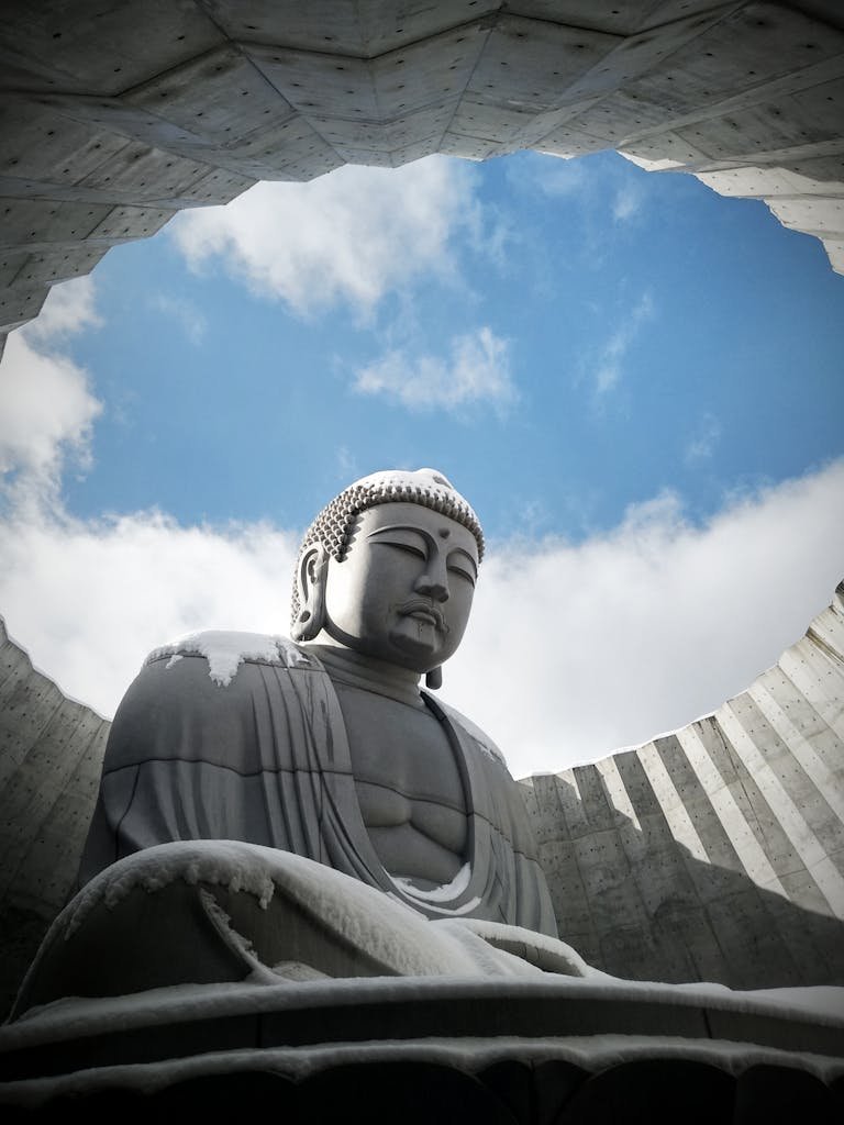 A serene Buddha statue covered in snow, set against a blue sky in Sapporo, Japan.