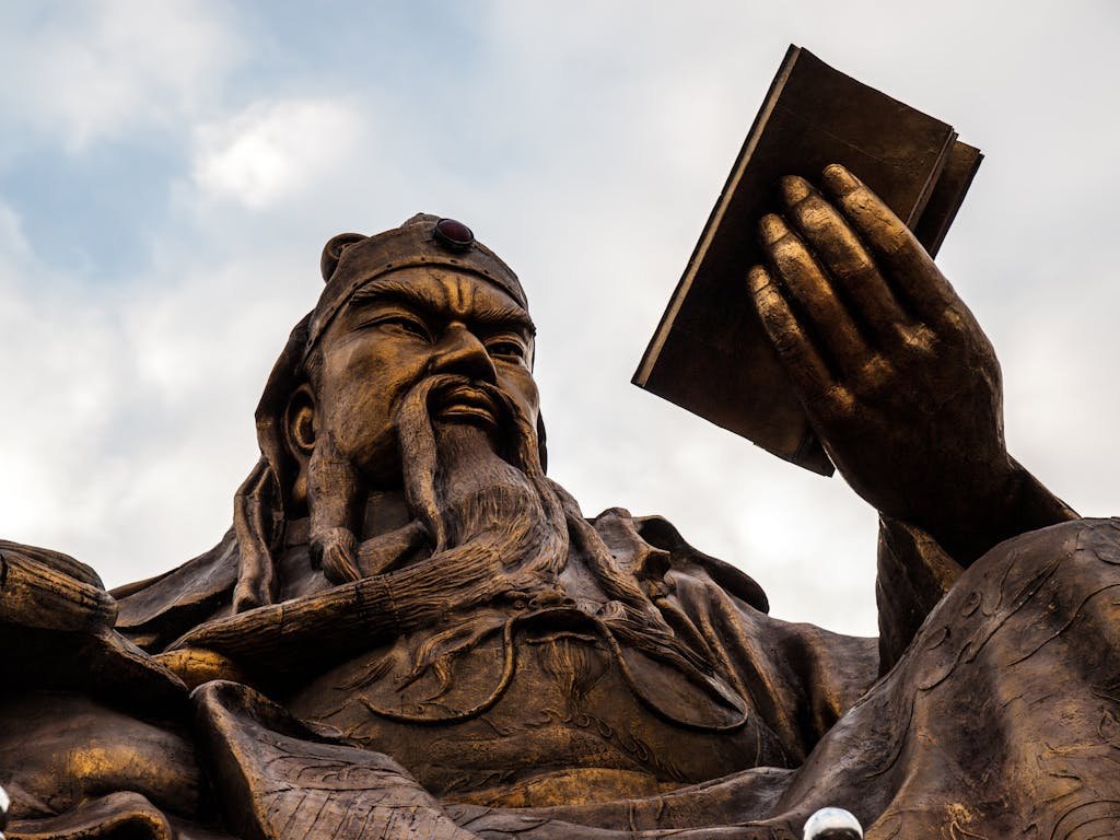 Bronze statue of Guan Yu representing strength and wisdom against cloudy sky.